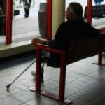 Male Native American sits with a crutch, waiting for a public bus
