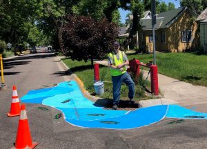 Volunteer poses with fish mural painted on Bozeman street as part of traffic calming project