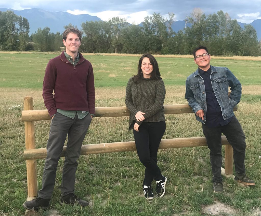Transportation Fellows Vince Ziols, Naomi Fireman, and Nathan Begay in field with mountain view near Kalispell, Montana.
