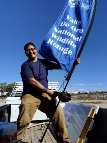 Nate Begay outside with flag that reads Valle de Oro National Wildlife Refuge