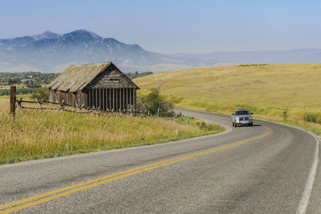 vehicle on two-lane rural highway near barn with mountains in background