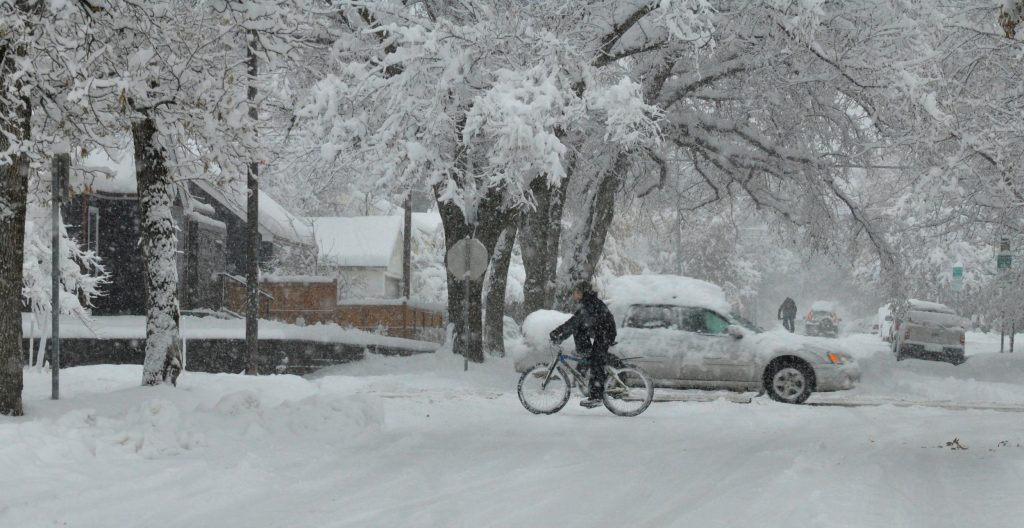 Bicyclist and car travel through neighborhood in heavy snow conditions