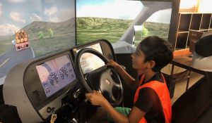 A young boy peers over the steering wheel of a driving simulator.