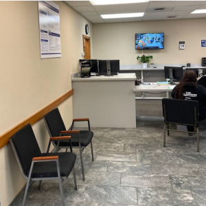 Two chairs sit along a wall in a waiting room. A TV hangs on the far wall.